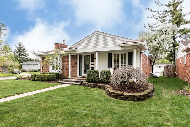 ranch-style house with brick siding, a chimney, a front yard, and a porch