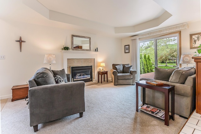 living room with a tray ceiling, a tile fireplace, light colored carpet, and baseboards