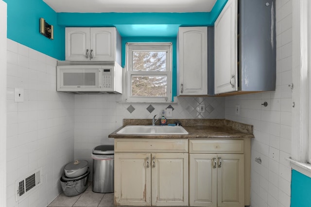 9069 Pierson St, Detroit, MI 48228 - kitchen with a sink, white microwave, tile walls, light tile patterned flooring, and dark countertops
