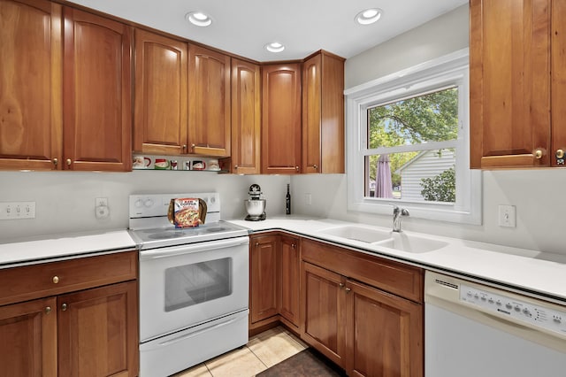 kitchen with white appliances, a sink, brown cabinetry, light countertops, and light tile patterned floors