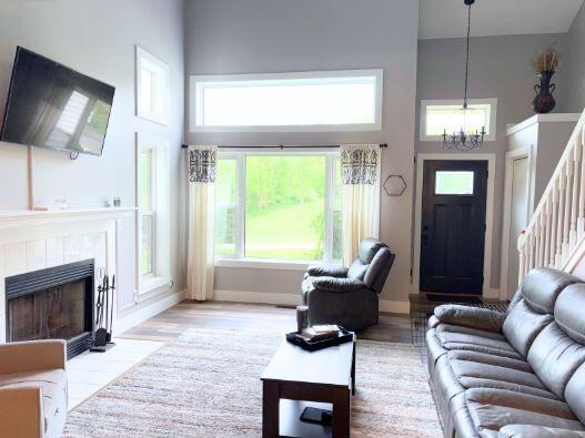 living area with a high ceiling, a chandelier, wood finished floors, a tiled fireplace, and baseboards