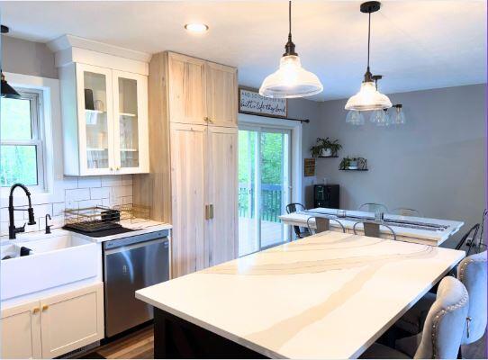 kitchen with stainless steel dishwasher, glass insert cabinets, light countertops, pendant lighting, and a sink