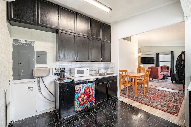 kitchen featuring a sink, white microwave, electric panel, backsplash, and light countertops