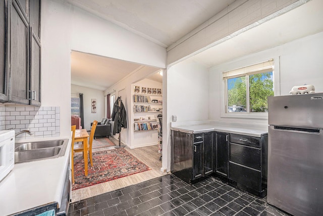 kitchen featuring freestanding refrigerator, vaulted ceiling, a sink, light countertops, and tasteful backsplash