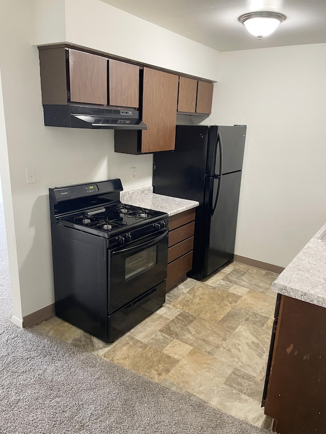 kitchen with black appliances, under cabinet range hood, light countertops, baseboards, and stone finish floors