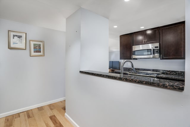 1300 E Lafayette St Unit 1604, Detroit, MI 48207 - kitchen featuring stainless steel microwave, dark stone counters, dark brown cabinets, light wood-style flooring, and recessed lighting