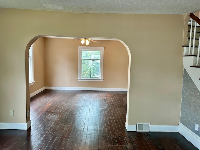 spare room featuring arched walkways, hardwood / wood-style flooring, a ceiling fan, stairway, and baseboards