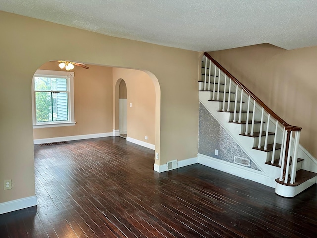 unfurnished living room with arched walkways, hardwood / wood-style flooring, a ceiling fan, stairway, and baseboards