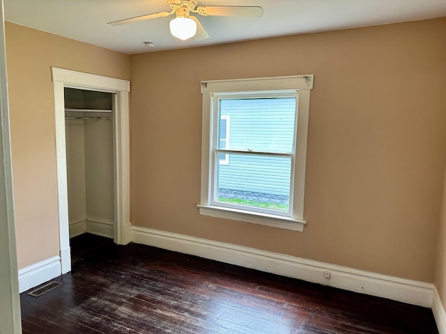 unfurnished bedroom with dark wood-style floors, a closet, baseboards, and a ceiling fan