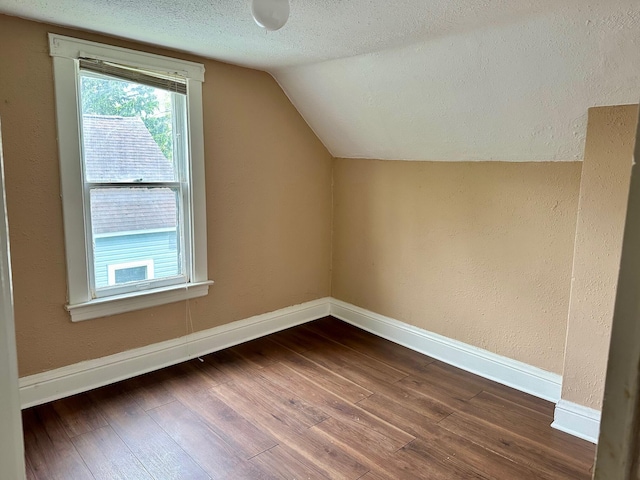 additional living space with dark wood-style flooring, lofted ceiling, baseboards, and a textured ceiling