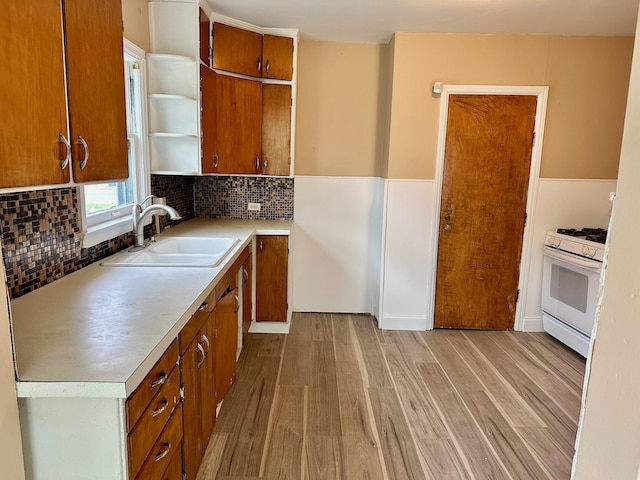 kitchen featuring white gas stove, a sink, light wood finished floors, open shelves, and light countertops