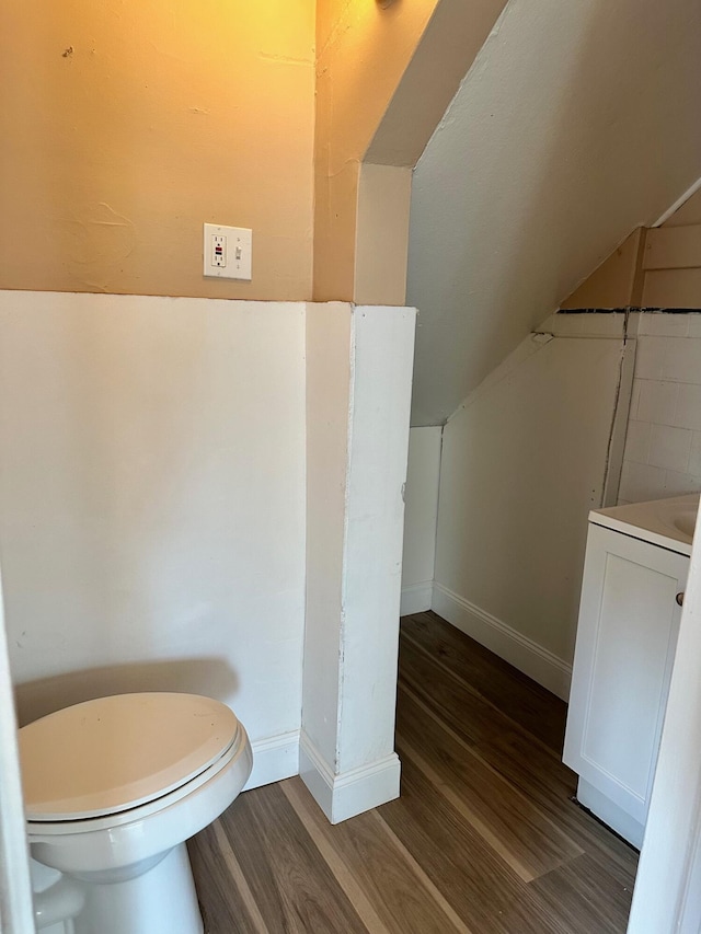 bathroom featuring wood finished floors, toilet, baseboards, vaulted ceiling, and vanity