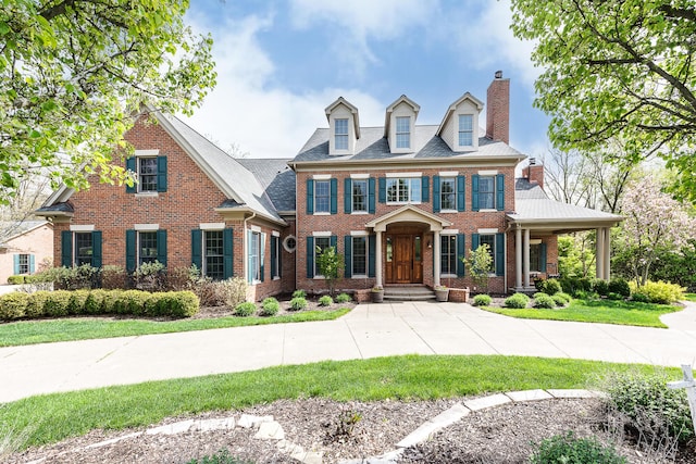 colonial inspired home with brick siding, a chimney, and a front yard