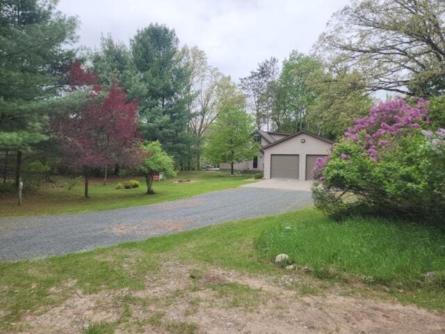 9332 W 10 Mile Rd, Irons, MI 49644 - exterior space featuring a garage, a front lawn, view of wooded area, and driveway