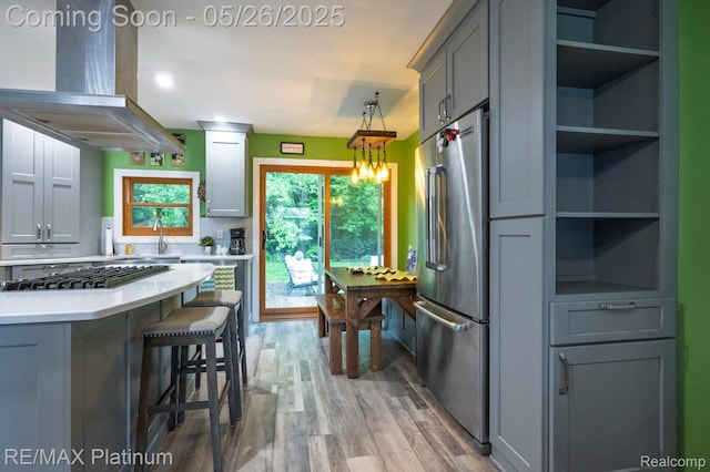 638 Glenwyth Rd, Brighton, MI 48116 - kitchen featuring stainless steel appliances, wall chimney range hood, light wood finished floors, light countertops, and a breakfast bar