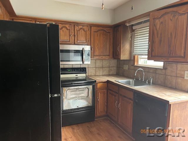 6730 Summerfield Rd, Temperance, MI 48182 - kitchen with black appliances, a sink, tile countertops, and backsplash