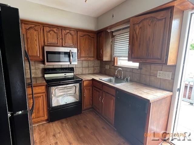 6730 Summerfield Rd, Temperance, MI 48182 - kitchen featuring black appliances, tile countertops, a sink, light wood-style flooring, and brown cabinets