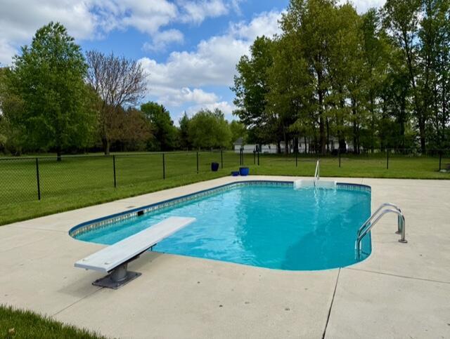view of pool featuring a diving board, a patio, and view of wooded area