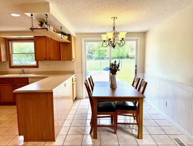dining area with a wainscoted wall, a chandelier, healthy amount of natural light, a textured ceiling, and light tile patterned floors