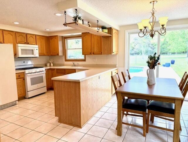 kitchen featuring white appliances, a peninsula, light countertops, a chandelier, and recessed lighting
