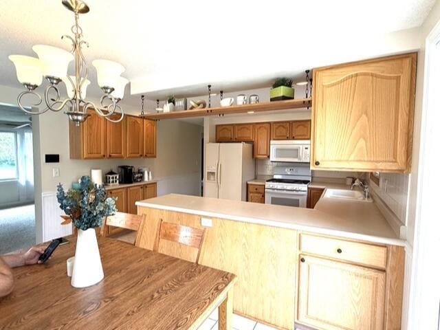 kitchen featuring white appliances, a chandelier, a sink, a peninsula, and light countertops