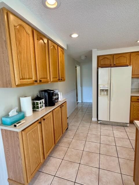 kitchen with white refrigerator with ice dispenser, light countertops, a textured ceiling, recessed lighting, and brown cabinetry