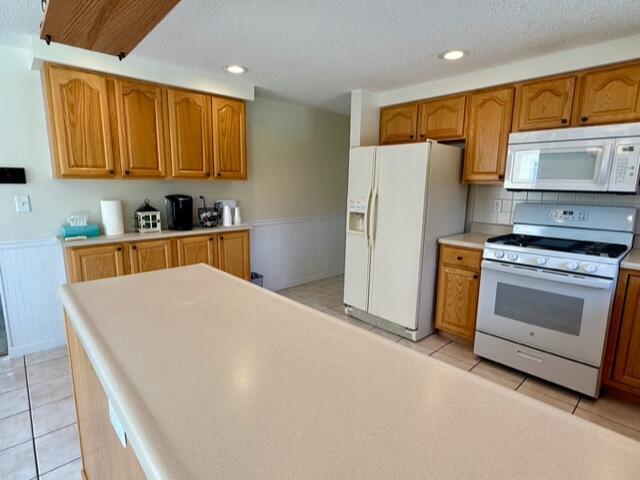 kitchen featuring white appliances, a wainscoted wall, brown cabinets, light tile patterned floors, and recessed lighting