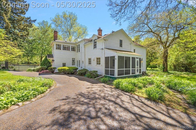 16109 E Jefferson Ave, Grosse Pointe Park, MI 48230 - rear view of property featuring a sunroom, a chimney, and asphalt driveway
