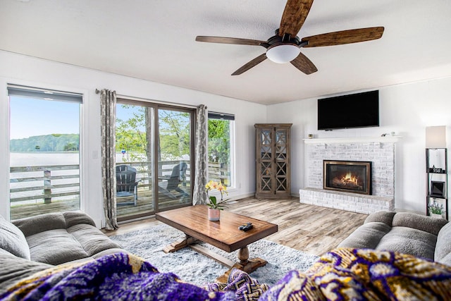 living room with a ceiling fan, wood finished floors, and a brick fireplace
