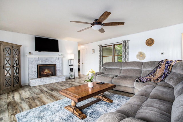 living room featuring a ceiling fan, wood finished floors, and a brick fireplace