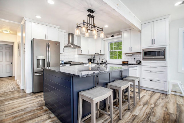 kitchen with wall chimney exhaust hood, stainless steel appliances, dark stone countertops, light wood-style floors, and recessed lighting