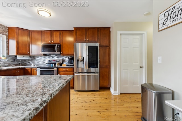 750 2nd St Unit 27, Wyandotte, MI 48192 - kitchen with stainless steel appliances, light wood-style flooring, decorative backsplash, light stone counters, and brown cabinetry