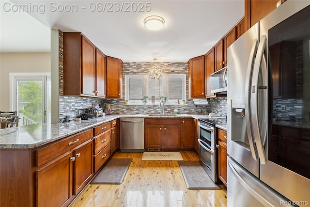 750 2nd St Unit 27, Wyandotte, MI 48192 - kitchen featuring appliances with stainless steel finishes, light wood-style flooring, tasteful backsplash, light stone counters, and brown cabinets
