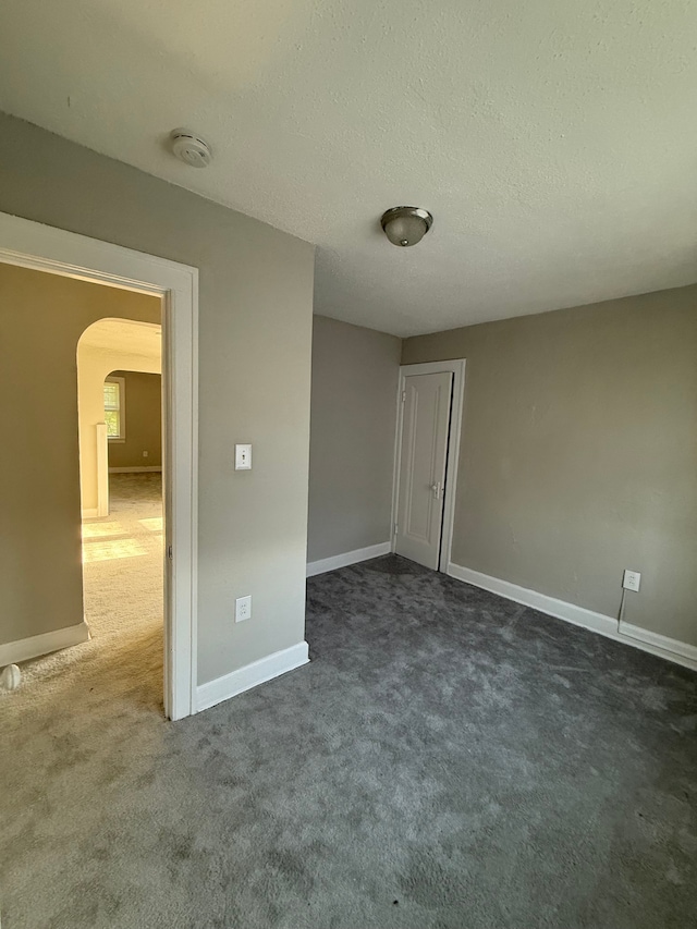 7130 Julian St, Detroit, MI 48204 - unfurnished bedroom featuring arched walkways, dark carpet, baseboards, a textured ceiling, and a closet
