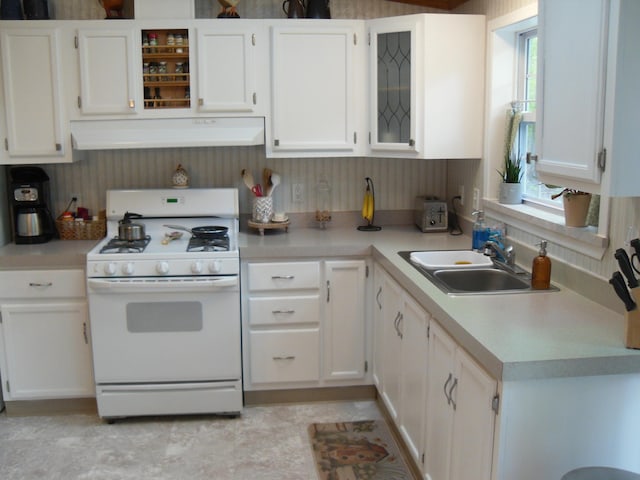 6515 Maple Rd, Ludington, MI 49431 - kitchen with white gas stove, a sink, under cabinet range hood, white cabinets, and light countertops