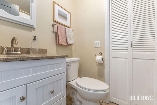 bathroom with toilet, vanity, and a closet