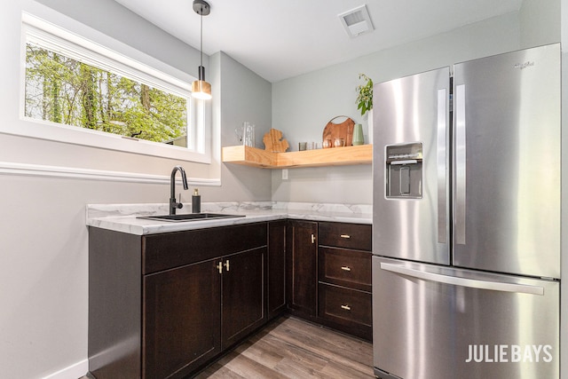 kitchen featuring stainless steel fridge, a sink, wood finished floors, dark brown cabinetry, and decorative light fixtures