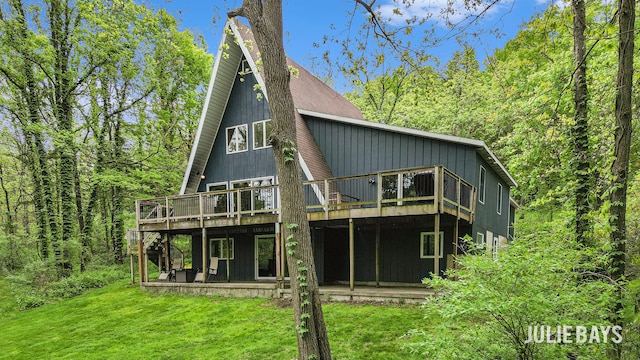rear view of house with a deck, a lawn, and a forest view