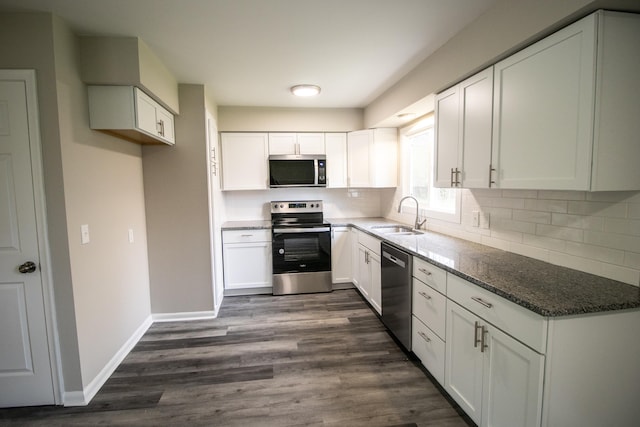 kitchen with stainless steel appliances, a sink, dark stone countertops, and white cabinetry
