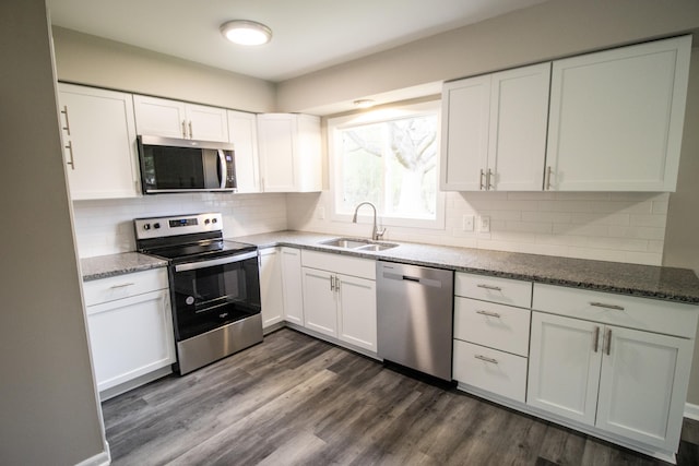 kitchen featuring stainless steel appliances, a sink, white cabinets, dark wood-style flooring, and stone countertops