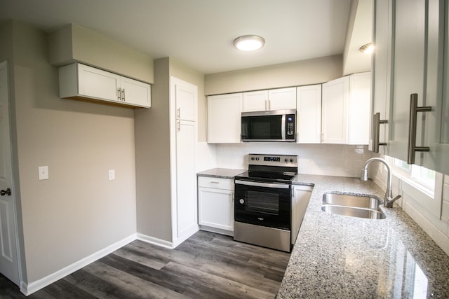 kitchen with stainless steel appliances, a sink, light stone counters, white cabinets, and backsplash
