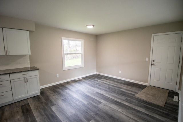 unfurnished dining area with baseboards and dark wood-style flooring