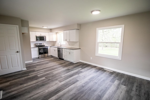 kitchen with appliances with stainless steel finishes, a sink, dark wood finished floors, baseboards, and white cabinetry