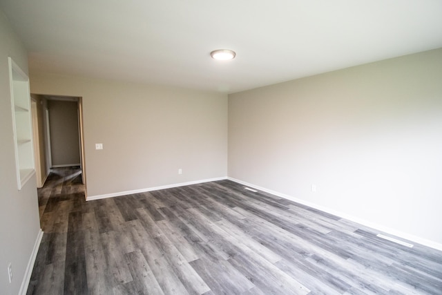 spare room featuring dark wood-style floors and baseboards