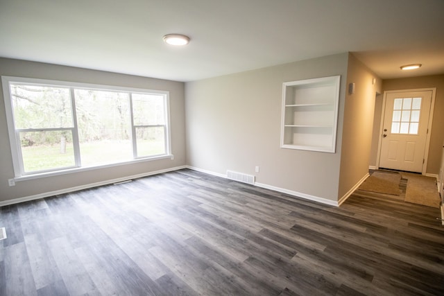 empty room featuring built in shelves, dark wood finished floors, baseboards, and plenty of natural light