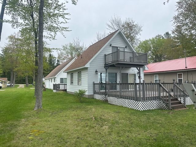 rear view of property featuring a balcony, a lawn, and a deck