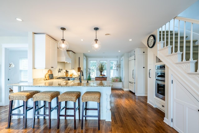 7881 Lakewood Dr, Coloma, MI 49038 - kitchen with a peninsula, light stone countertops, double oven, white cabinetry, and custom range hood