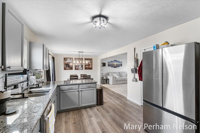 kitchen featuring gray cabinetry, a peninsula, appliances with stainless steel finishes, a sink, and light wood-style floors