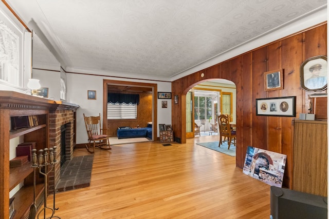 449 Spruce St, Wyandotte, MI 48192 - living room with arched walkways, wooden walls, light wood-type flooring, crown molding, and a brick fireplace