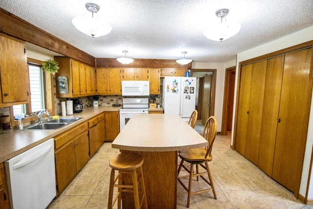 kitchen with white appliances, a textured ceiling, brown cabinets, a sink, and a kitchen island